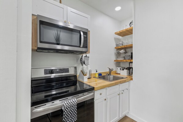 Una cocina moderna con armarios blancos, un microondas de acero inoxidable, un horno negro y una encimera de madera.