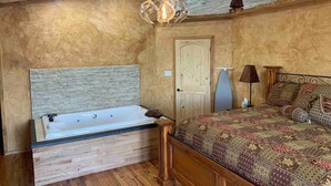 Un dormitorio con cabecera de madera, una cama grande con ropa de cama estampada, una mesita de noche con lámpara y una puerta de madera.