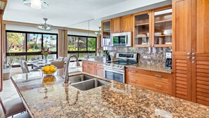 Cozinha moderna com bancadas de granito, eletrodomésticos de aço inoxidável, armários de madeira e uma grande janela com vista para um jardim.