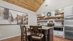 Una cocina con armarios de madera, un refrigerador de acero inoxidable, un microondas y un comedor con dos sillas.