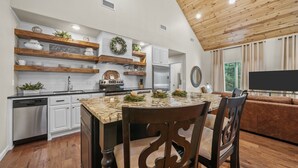 Una cocina moderna con armarios blancos, estantes de madera y encimera de granito.