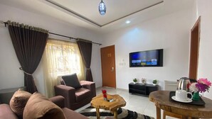 A living room with a sofa, armchair, coffee table, TV, and a small table with a tray. - BINTOO HOTEL LIMITED (Sagamu)