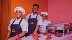 Three individuals in chef attire standing behind a buffet table with folded napkins and a silver buffet cart. - BINTOO HOTEL LIMITED (Sagamu)