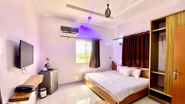 A modern bedroom with a bed, bedside table, TV, and wardrobe. - BINTOO HOTEL LIMITED (Sagamu)