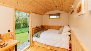 Una habitación de madera con cama, una mesita y ventana con vista a un jardín.