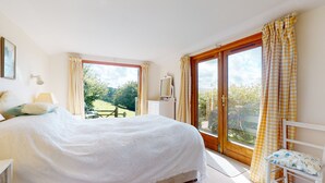 A bedroom with a large bed, a bedside table, a chair, and a window with curtains. - Hillway Lodge, Withypool (Withypool)
