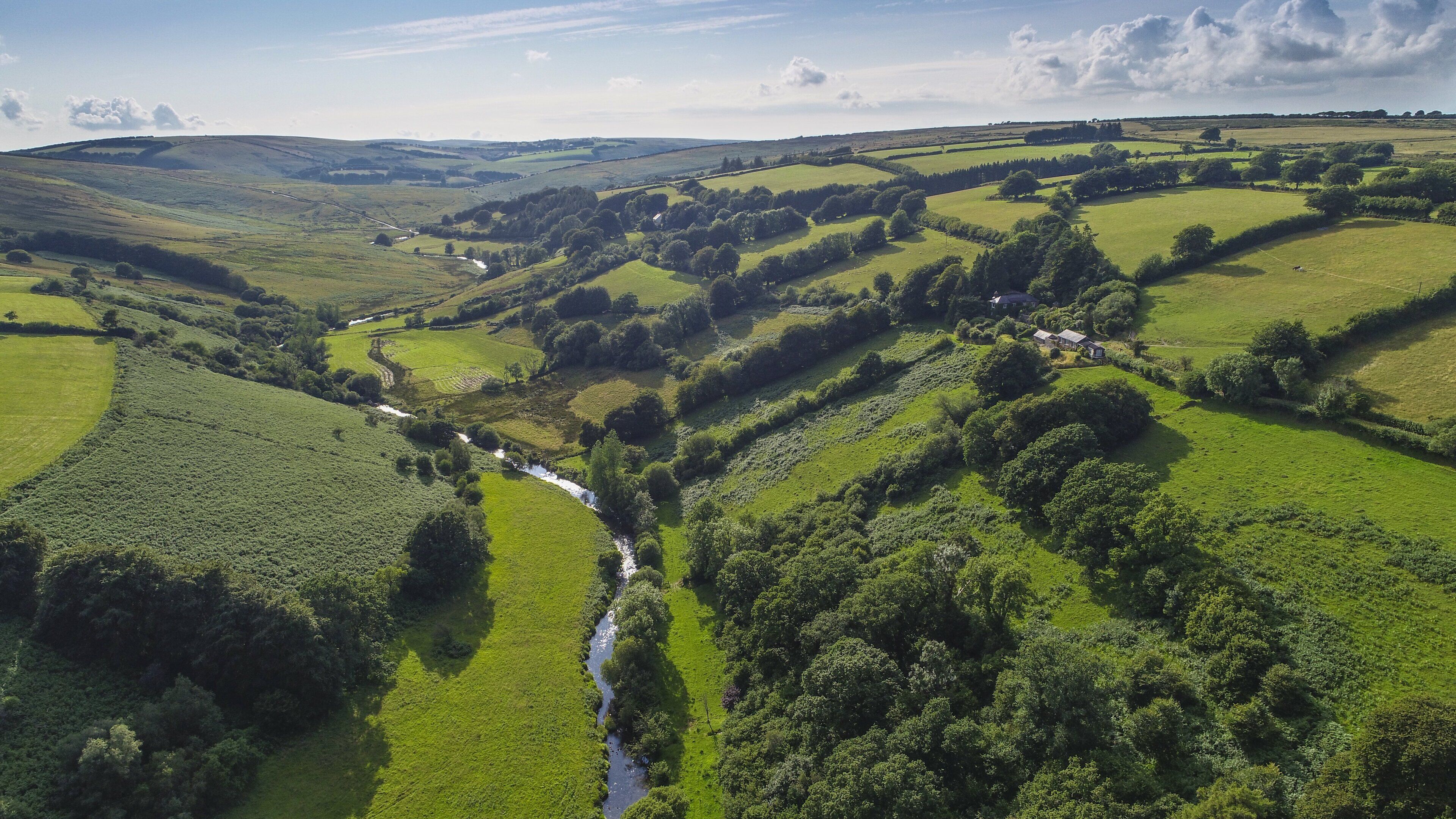 A rural landscape with rolling hills, a river, and scattered trees.