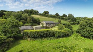 A stone house with a sloped roof, surrounded by lush greenery and a clear sky. - Hillway Lodge, Withypool (Withypool)