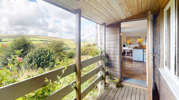 A wooden balcony with a view of rolling hills and a rustic interior with a kitchen area. - Hillway Lodge, Withypool (Withypool)