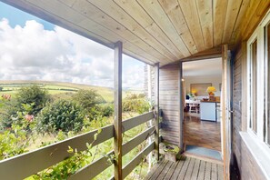 Un balcón de madera con vistas a colinas ondulantes y un interior rústico con una zona de cocina.