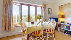 A dining area with a table and chairs, a bookshelf, and a window with curtains. - Hillway Lodge, Withypool (Withypool)