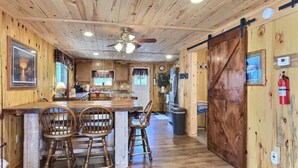 A rustic cabin interior with a wooden dining area, a kitchen, and a large sliding door.