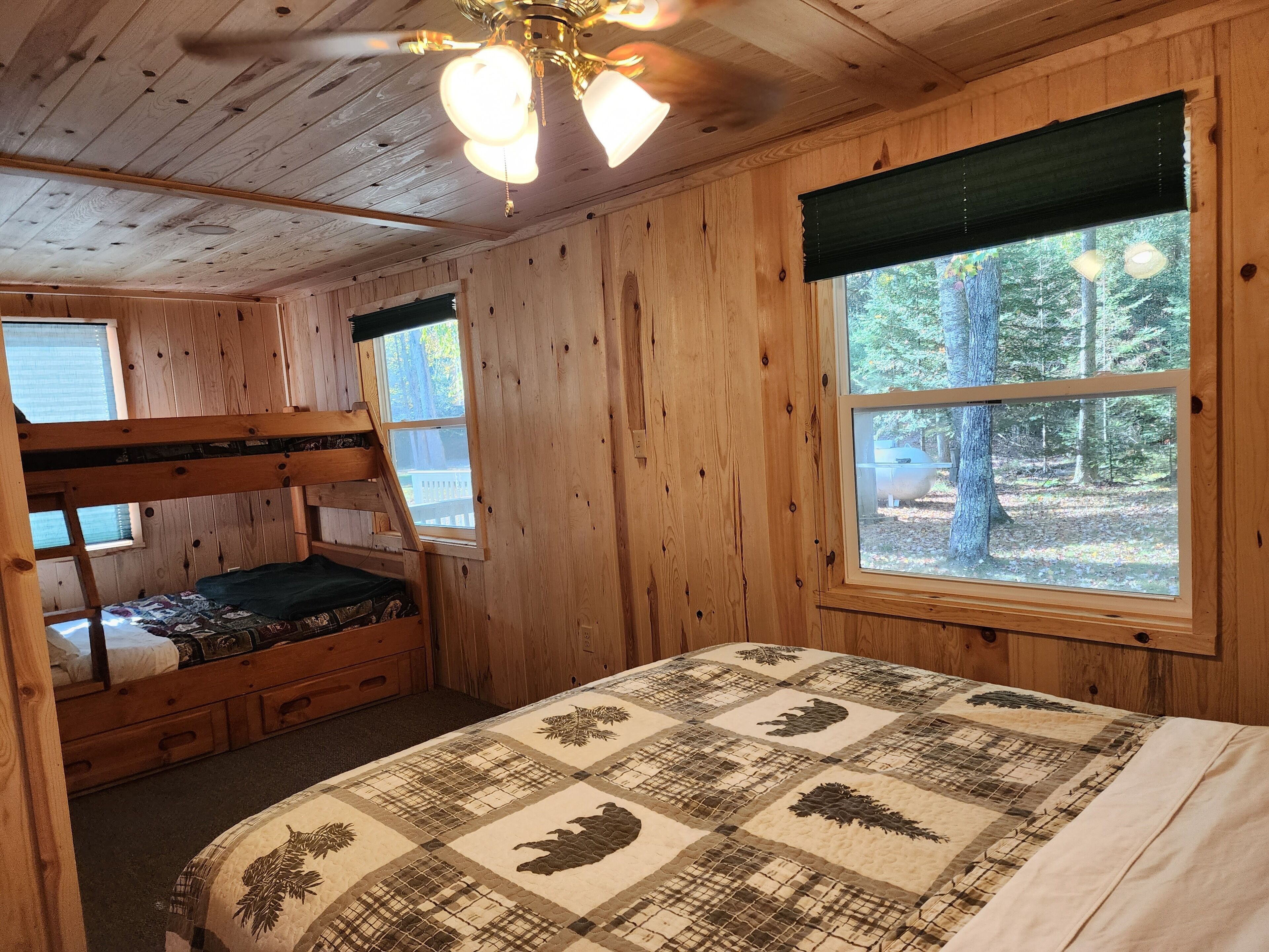 Ein Schlafzimmer einer Holzhütte mit Etagenbetten, einer gesteppten Bettdecke und einem großen Fenster mit Blick auf den Wald.