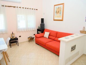 A living room with a red sofa, a white table, a small black TV stand, and a framed picture on the wall. - 2 Bed Apartment Sleeps 4 with Free Parking (Durres)