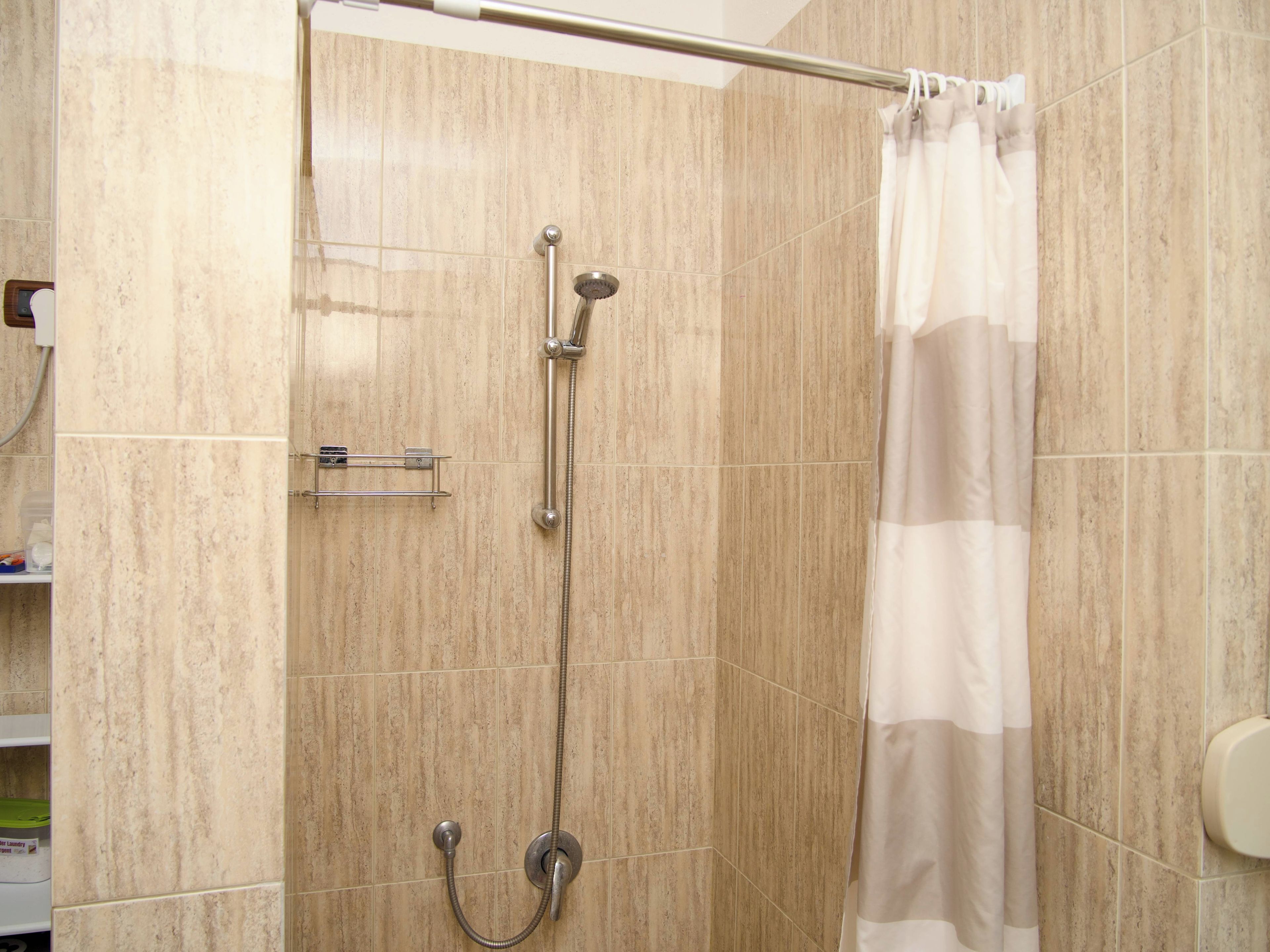 A shower with a handheld showerhead and a fixed showerhead, a towel rack, and a shower curtain.