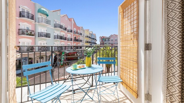 Un balcon avec des chaises bleues et une table, d’où l’on peut admirer des bâtiments aux couleurs vives et une rue animée.