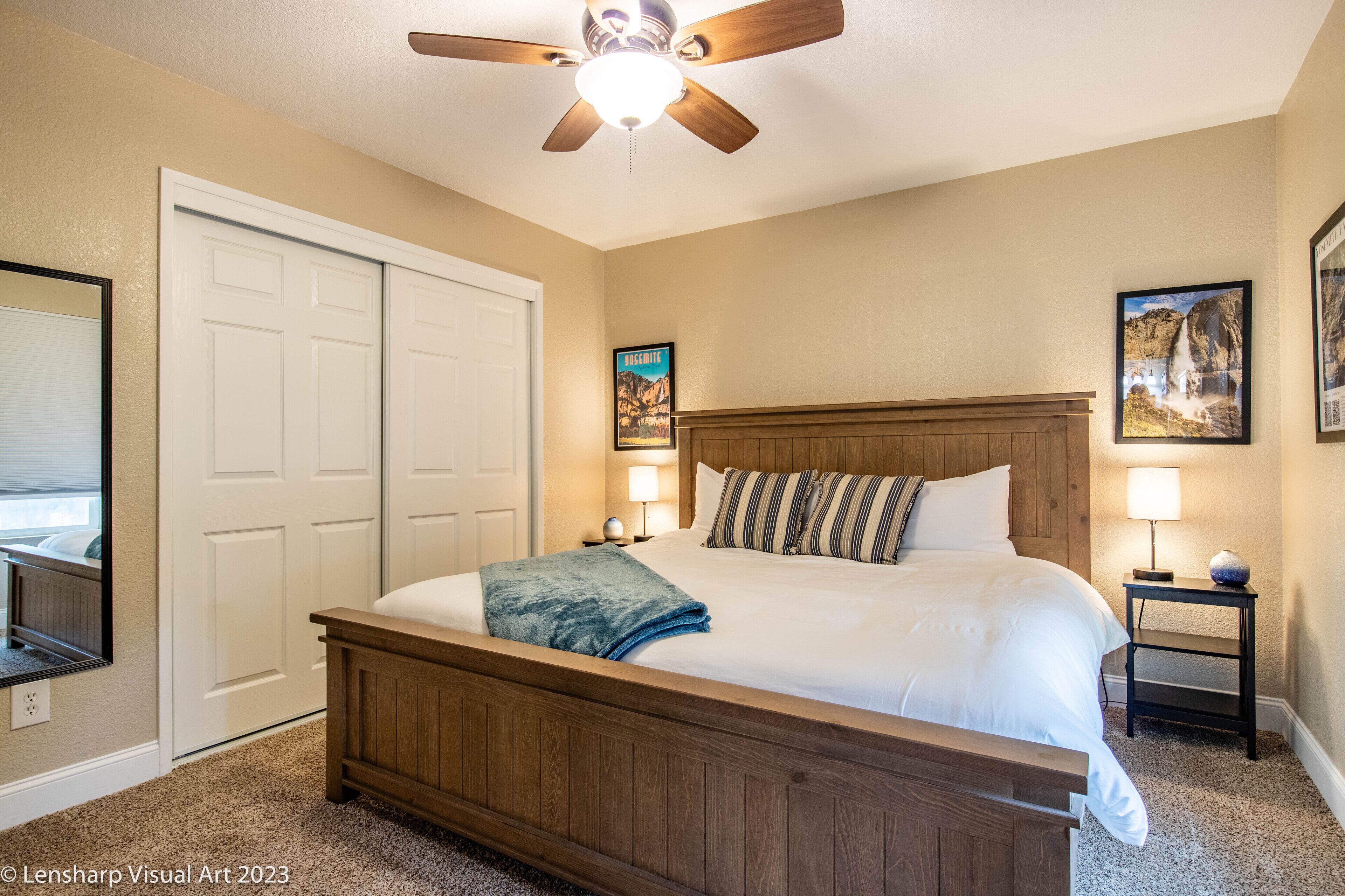 A bedroom with a wooden bed, a ceiling fan, a white door, and two wall-mounted lamps.