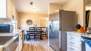 A modern kitchen with stainless steel appliances, a dining area with wooden chairs, and a white countertop. - Fantastic Views w/ Hottub,  Firepit & Horseshoes (Ahwahnee)