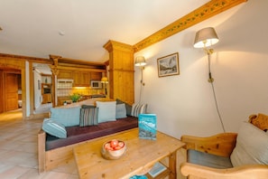 Un salon chaleureux avec un canapé en bois, une table en bois sur laquelle se trouve un bol de pommes, et un livre intitulé « CHANONIS MONTBLANC ».