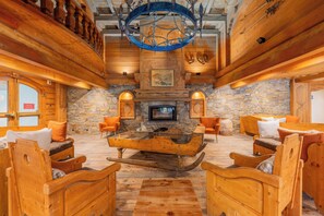 A log cabin interior with a stone fireplace, wooden furniture, and a chandelier.
