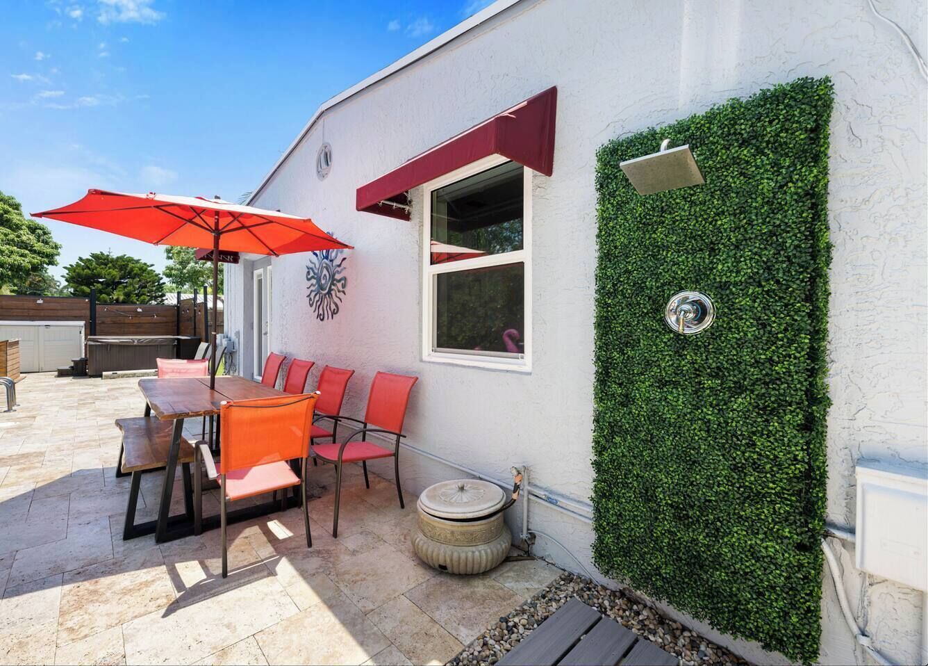 Eine Terrassengruppe im Freien mit Tisch und Stühlen, einem roten Sonnenschirm und einer mit Grünpflanzen bewachsenen Wand.