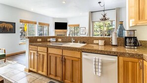 A modern kitchen with granite countertops, wooden cabinets, a built-in dishwasher, and a large window providing natural light. - Bright 3BD Kings Beach Townhome (Kings Beach)