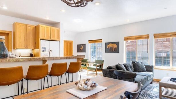A modern kitchen with wooden cabinets, a dining area with a wooden table and chairs, and a living room with a sofa and chairs. - Bright 3BD Kings Beach Townhome (Kings Beach)