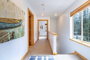 Ein Flur mit Holzboden, einem Gemälde eines Bootes an der linken Wand, einem Spiegel an der rechten Wand und einem Fenster mit Blick auf Bäume.