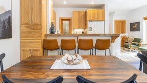 A modern kitchen with wooden cabinets, a central island, and a dining area with a wooden table and chairs. - Bright 3BD Kings Beach Townhome (Kings Beach)