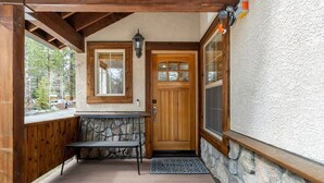 A wooden porch with a stone bench, a wooden door with glass panels, and a stone wall. - Bright 3BD Kings Beach Townhome (Kings Beach)