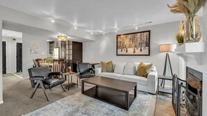 Ein modernes Wohnzimmer mit einer Couch, einem Couchtisch und Sesseln. Es gibt einen Kamin, einen Essbereich und ein Bild an der Wand.