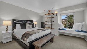 Ein Schlafzimmer mit Bett, Nachttischen, einer Bank, einer Sitzgelegenheit am Fenster und einem Wandregal.