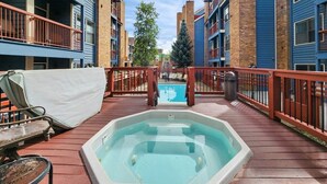 Un área de piscina en la azotea con jacuzzi, sillones de descanso y vistas de los edificios circundantes.