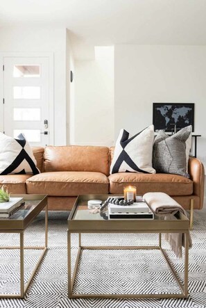 A living room with a brown leather sofa, two glass-top coffee tables, and patterned floor tiles. - Family-friendly Nashville home near Belmont, sleeps 10 with bunk room (Nashville)