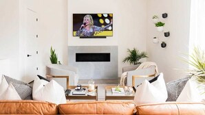 Ein modernes Wohnzimmer mit einem wandmontierten Flachbildfernseher, einem Kamin und einer gemütlichen Sitzecke mit Ledersofas und Kissen.