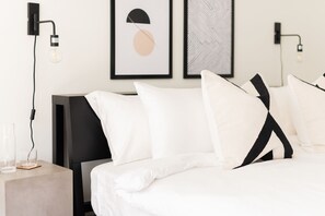 A modern hotel room with a bed, a bedside table, and a wall-mounted lamp. - Nashville rooftop fire pit home, sleeps 10 across 3 bedrooms (Nashville)