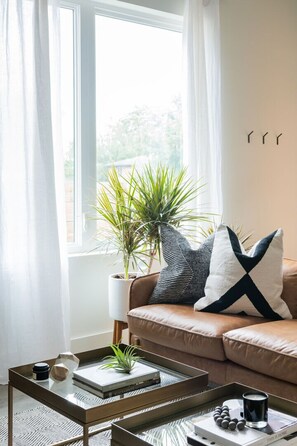 A living room with a brown leather sofa, a coffee table with a plant, and a window with curtains. - Downtown Nashville family home, sleeps 10, 3 bedrooms, gourmet kitchen (Nashville)