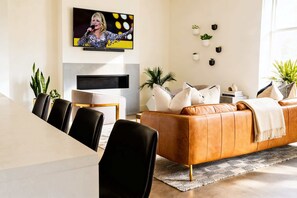 A modern living room with a leather sofa, a dining table with chairs, a flat-screen TV mounted on the wall, and several potted plants. - Summer rooftop deck, gourmet kitchen, parking near Broadway (Nashville)