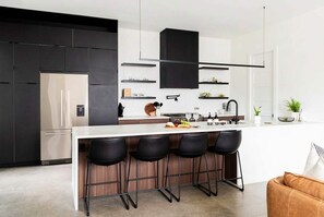 A modern kitchen with a central island, bar stools, and built-in appliances. - Family-friendly Nashville home near Belmont, sleeps 10 with bunk room (Nashville)