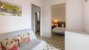 A room with a sofa, a bed, a small table, and a painting on the wall.