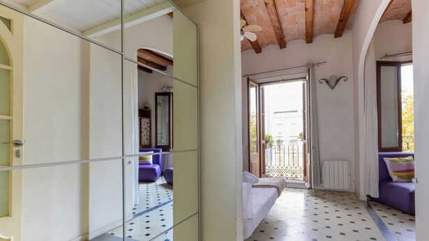 A room with a tiled floor, a bed with white bedding, a purple sofa, and a glass partition.