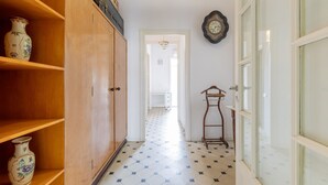 A hallway with wooden shelves, a tiled floor, a wooden door, and a wall clock.