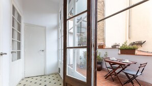 A room with a tiled floor, a wooden door, and a window. There is a table with chairs outside on a tiled patio.