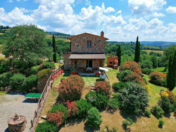 Una casa in pietra con un giardino, immersa tra colline e alberi.