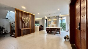 A modern interior with a wooden reception desk, a dining area with a table and chairs, and a staircase leading to an upper level. - Beach villa 3BR private swimming pool (Phu Quoc)