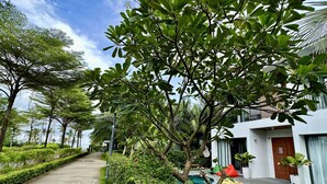 A pool area with a clear view of the pool, a yellow float, and a red chair. There is a pathway lined with greenery and a building with a white facade in the background. - Beach villa 3BR private swimming pool (Phu Quoc)