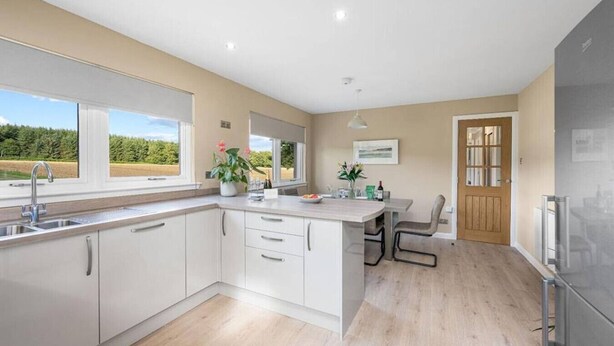 A modern kitchen with a large island, white cabinetry, and a view of the outdoors. - Muirton Cottage - Rural Bliss (Angus)