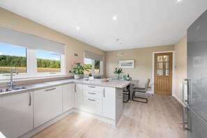 A modern kitchen with a large island, white cabinetry, and a view of the outdoors. - Muirton Cottage - Rural Bliss (Angus)