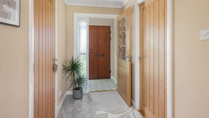 A hallway with wooden doors, a potted plant, and a patterned rug. - Muirton Cottage - Rural Bliss (Angus)