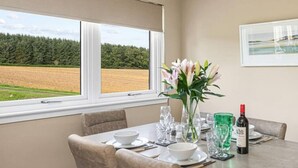 A dining area with a table set for four, a vase of flowers, and a bottle of wine. - Muirton Cottage - Rural Bliss (Angus)